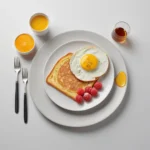 A beautifully plated breakfast with sunny-side-up egg toast, fresh raspberries, orange juice, and a drizzle of syrup on a white plate.